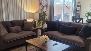 Una sala de estar con dos sofás, una mesa de centro, alfombra, una planta y un ventanal con cortinas.