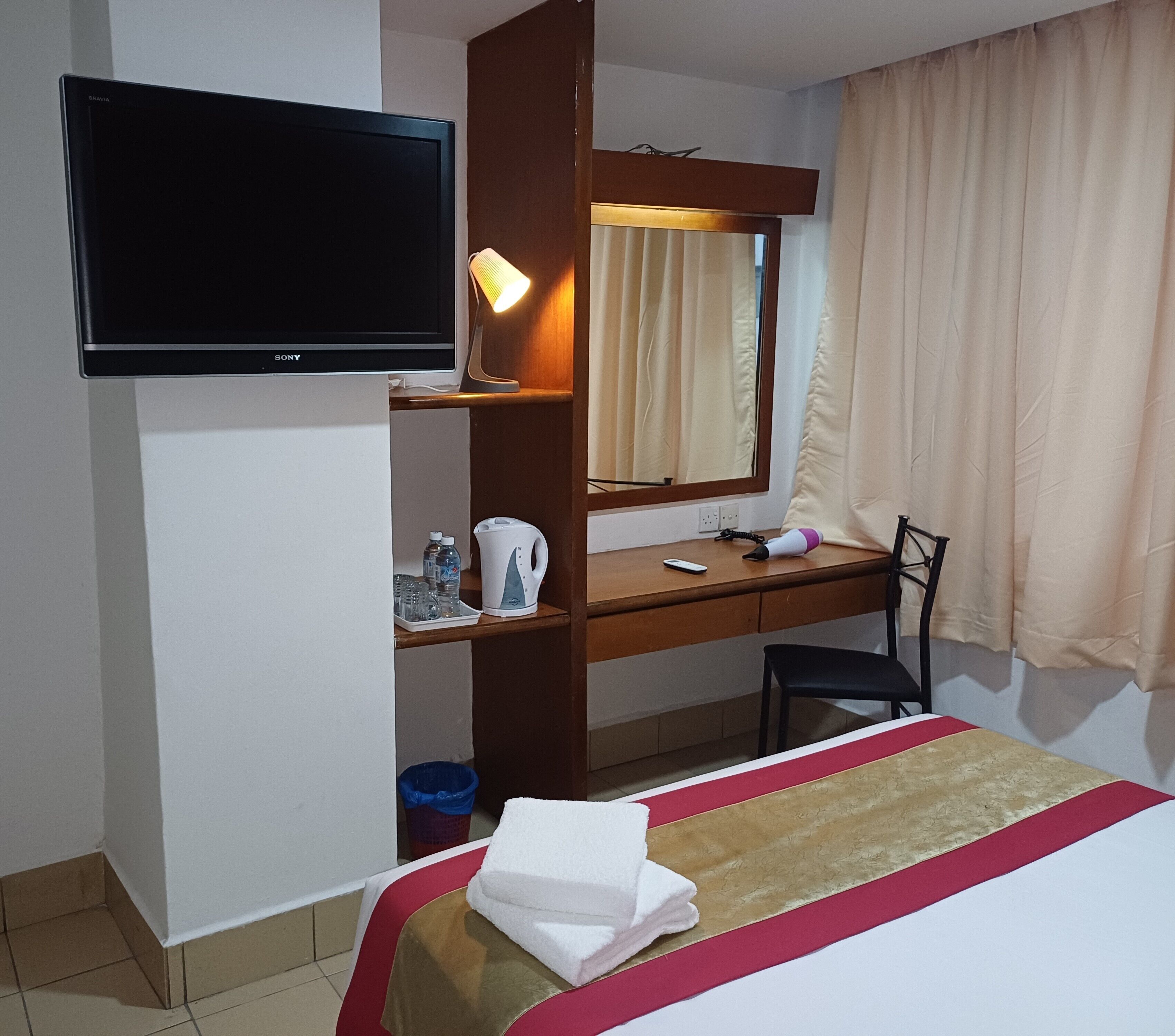 A hotel room with a bed, a desk, a television, a mirror, a lamp, a chair, and a window with curtains.