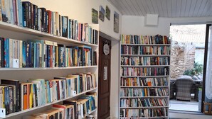 Une bibliothèque avec des étagères remplies de livres, un sol à carreaux et une porte sur laquelle est apposée une pancarte.