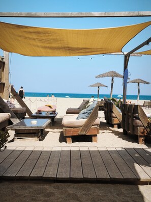 Un espace de détente aménagé sur la plage, avec des meubles en bois, un auvent et des parasols en chaume.