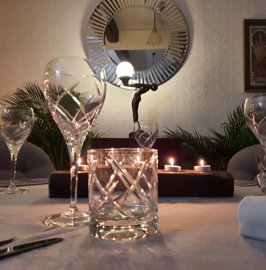 A dining area with a round mirror, a candle, and crystal glassware on a table.
