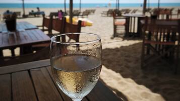 A beachside restaurant with outdoor seating, a glass of water, and umbrellas providing shade.