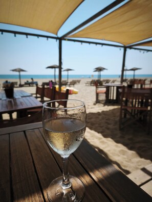 A beachside restaurant with outdoor seating, a glass of water, and umbrellas providing shade. - Maison du Coquelicot (Tourouzelle)