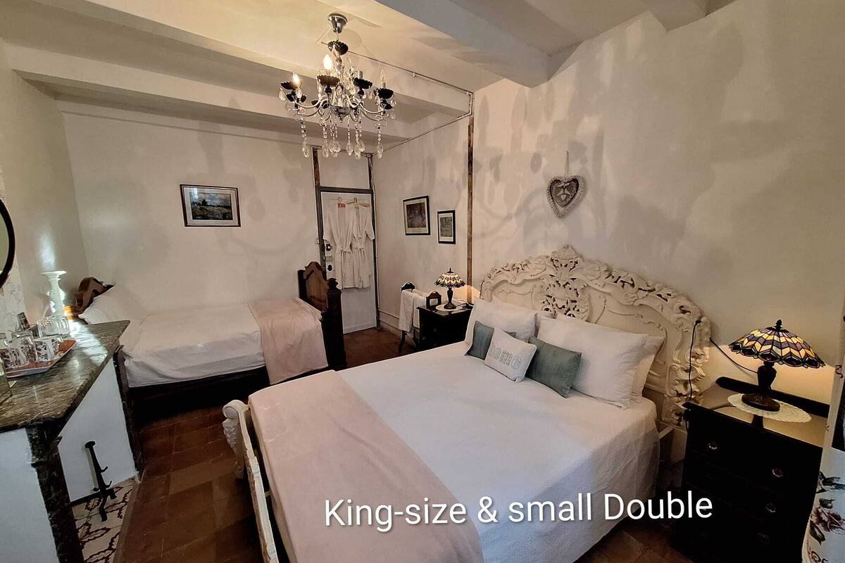 Een kingsize bed met een klein tweepersoonsbed in een kamer met een kroonluchter, een hartvormige decoratie aan de muur en een spiegel links.