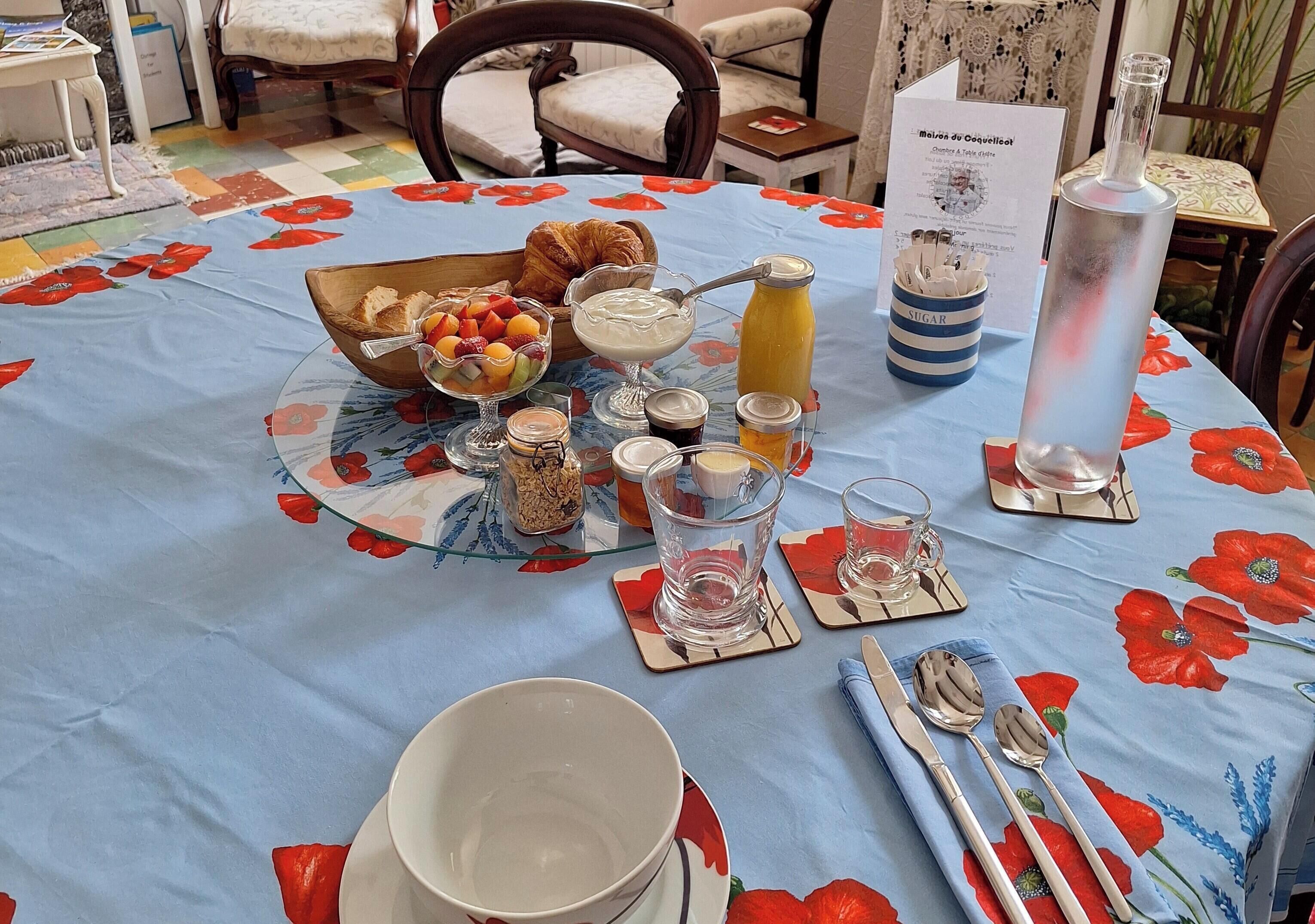 A breakfast table set with a variety of food items, including a bowl of fruit, a croissant, and a glass of orange juice.