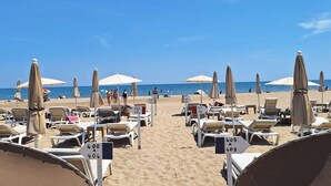 Une plage bordée de rangées de chaises longues et de parasols, des panneaux numérot és indiquant les différentes zones de la plage, et un ciel bleu azur.