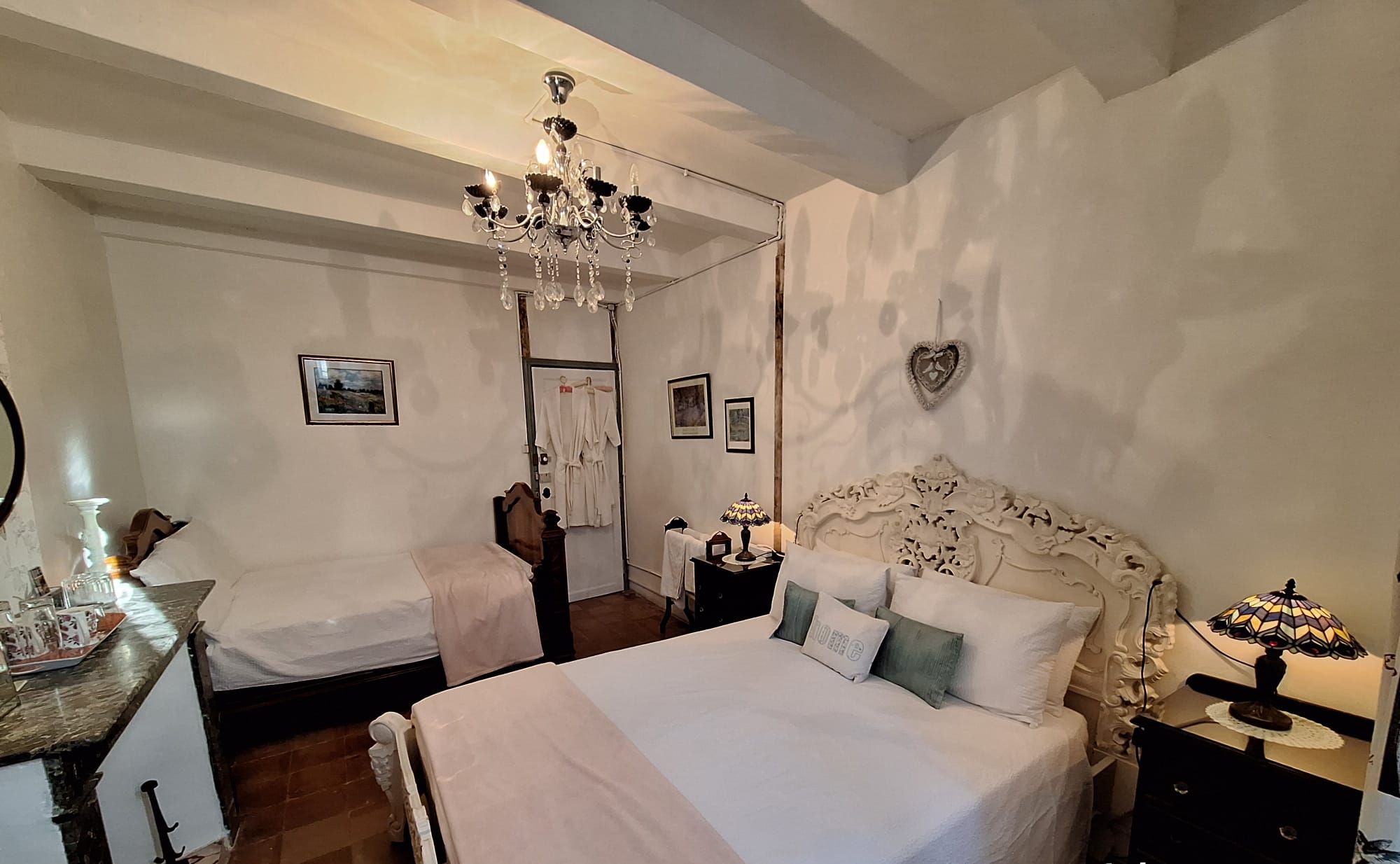 Una cama tamaño king con una cama doble pequeña en una habitación con un candelabro, un adorno con forma de corazón en la pared y un espejo a la izquierda.