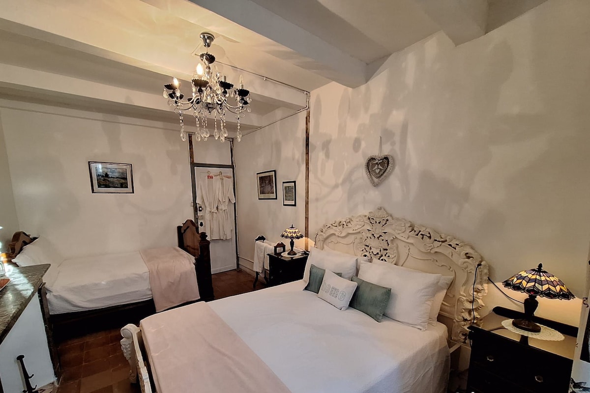 A king-size bed with a small double bed in a room with a chandelier, a heart-shaped decoration on the wall, and a mirror on the left.