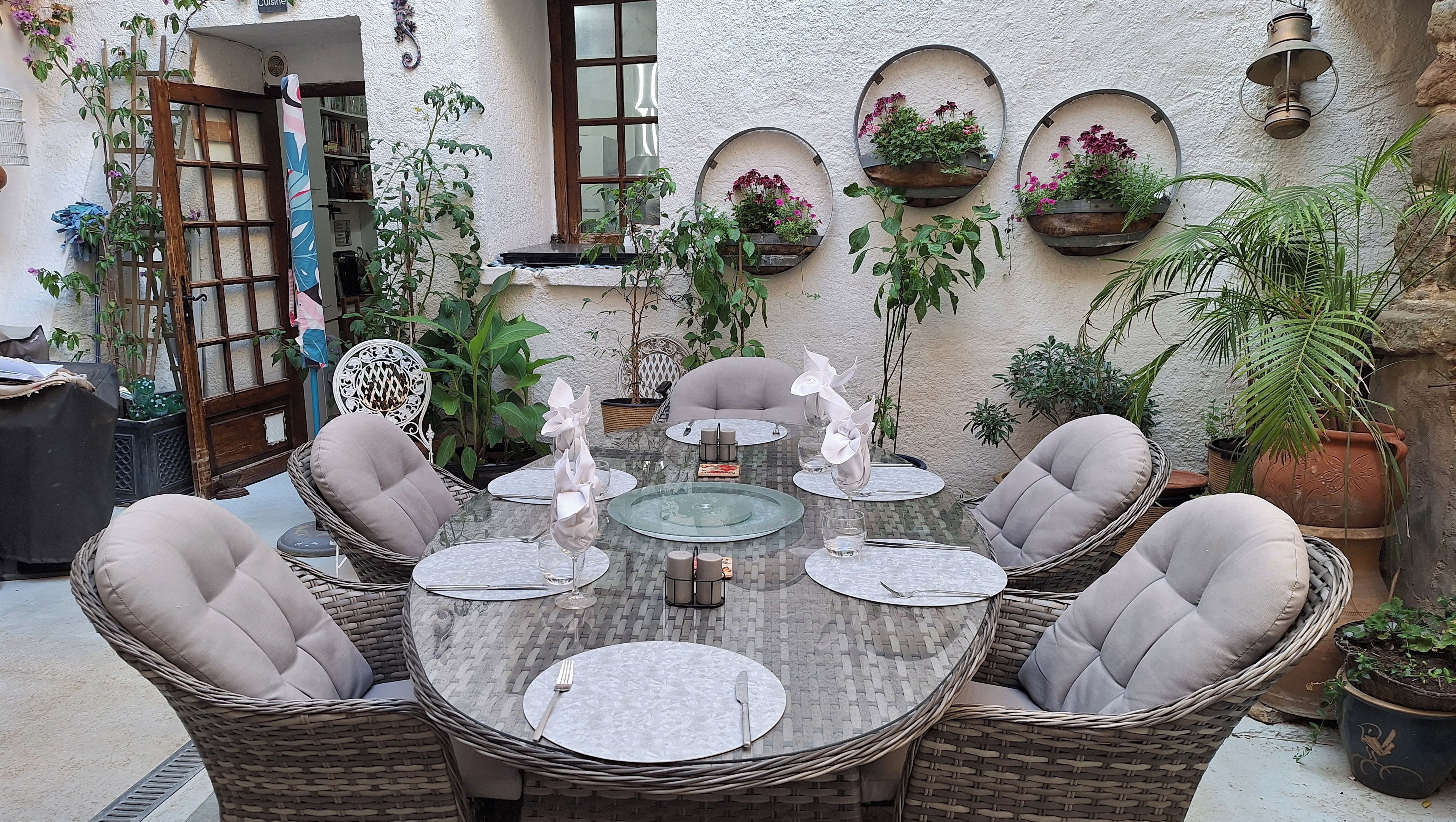 A dinner setup in a courtyard with wicker chairs, a glass table, and potted plants.
