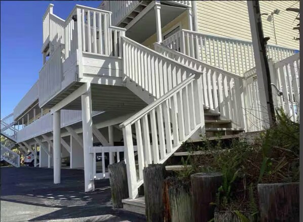 A multi-story building with a white exterior, multiple balconies, and a staircase leading to the entrance. - Cozy, Beachy, King Bed| Walk to Beach | Bring Fido (Gulf Shores)
