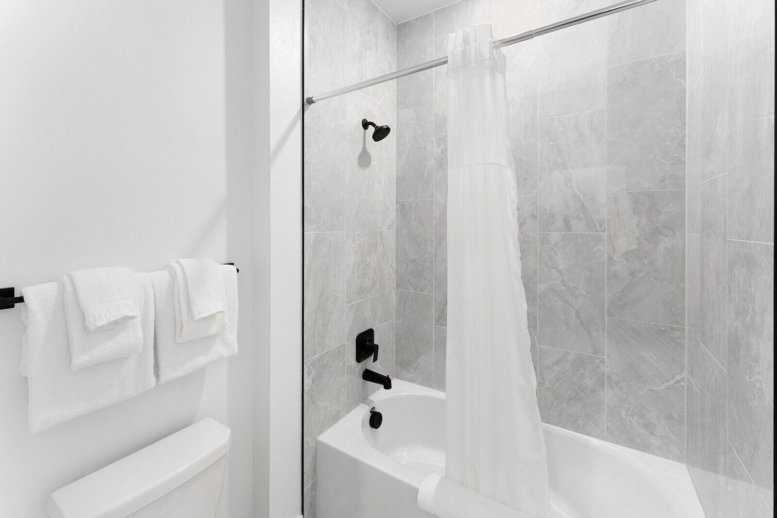 A modern bathroom with a glass shower enclosure, a white bathtub, and a towel rack with folded towels.