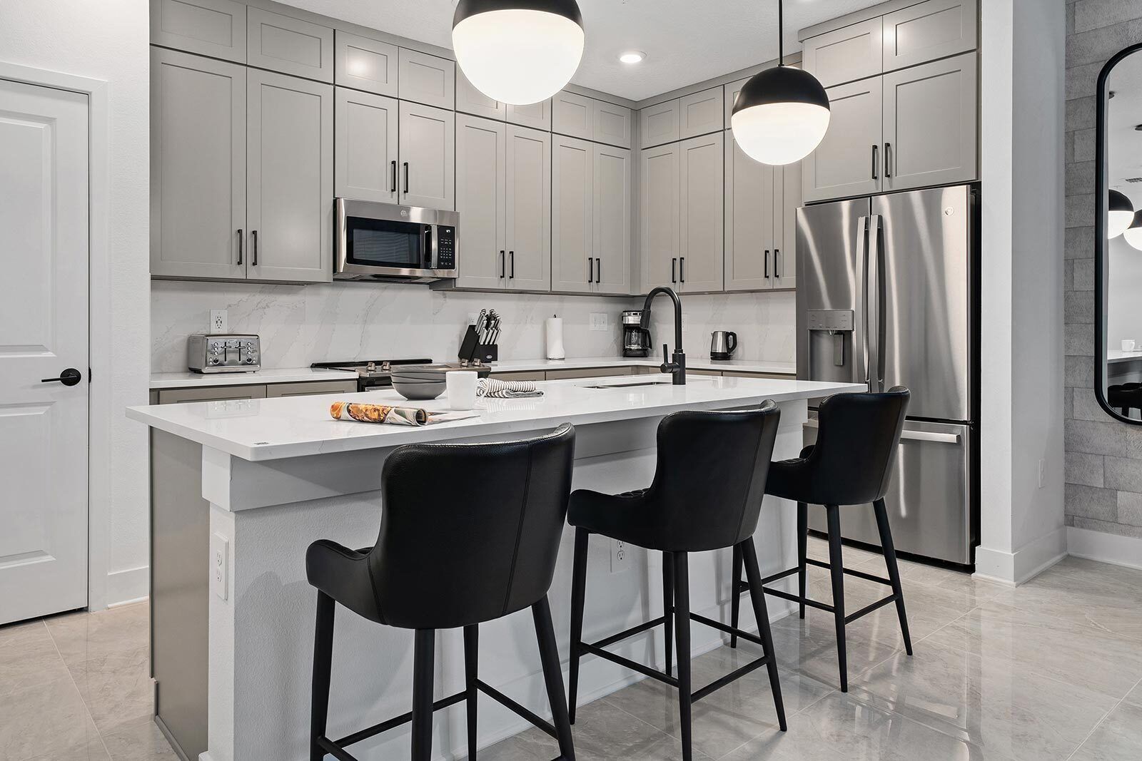 A modern kitchen with a central island, stainless steel appliances, and black bar stools.