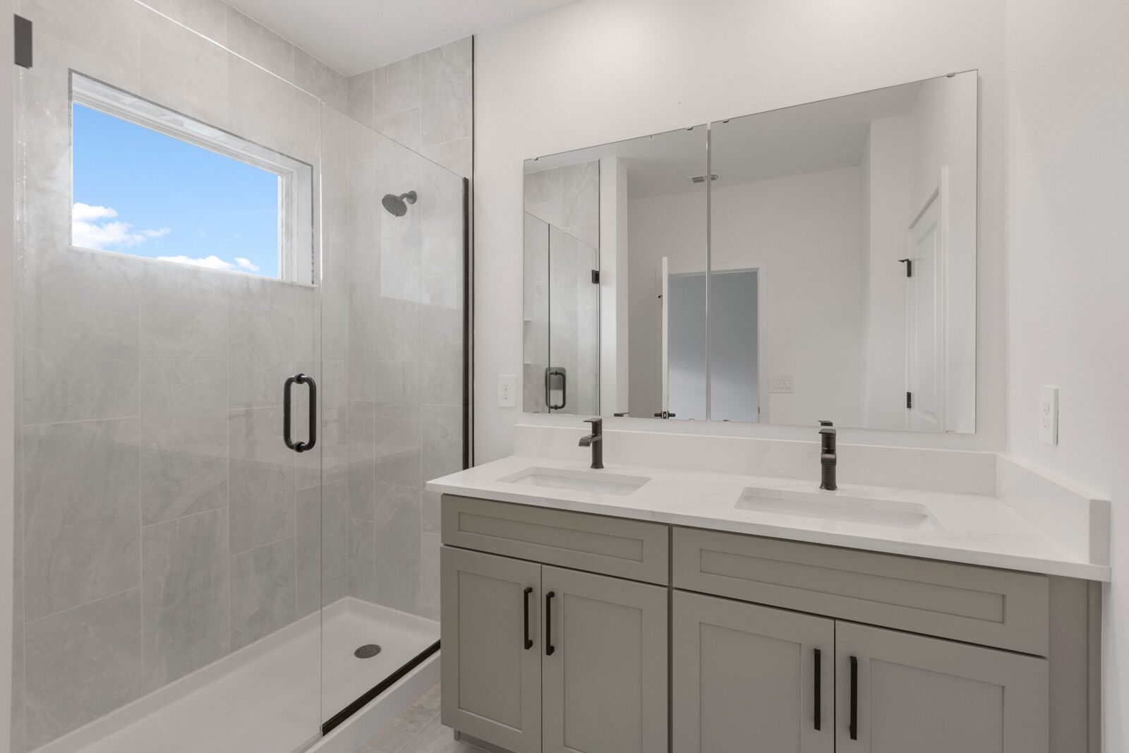A modern bathroom with a glass-enclosed shower, two sinks, a large mirror, and light-colored cabinetry.