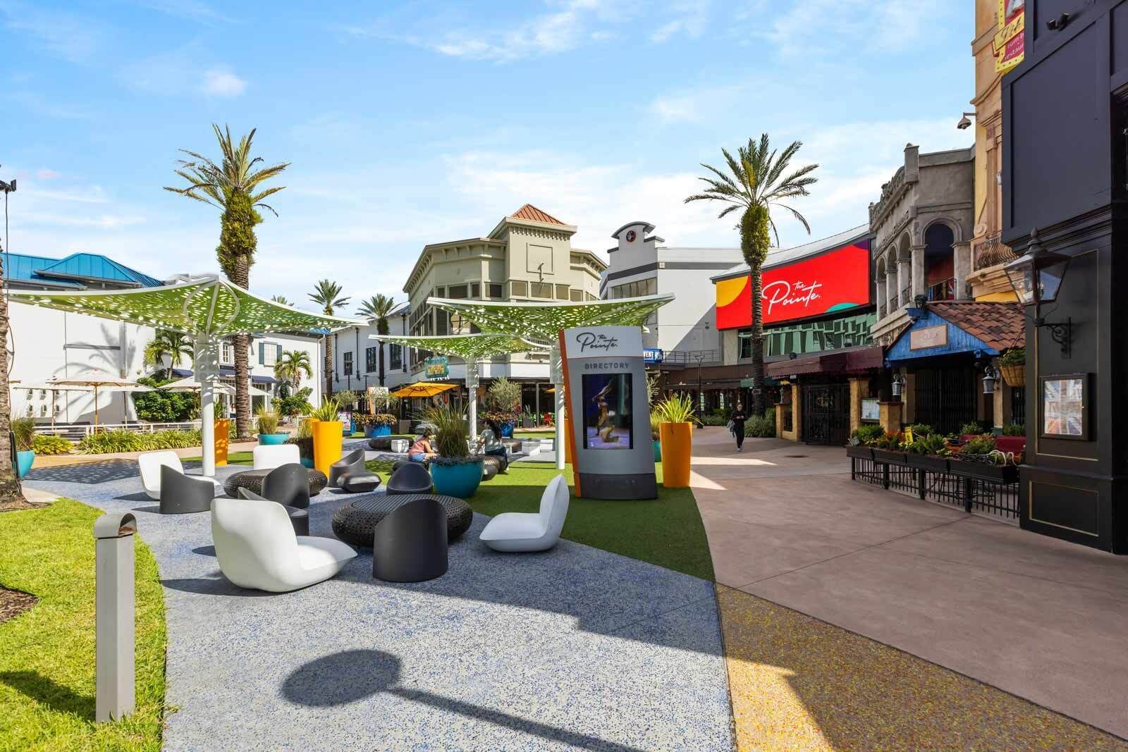 An outdoor seating area with modern chairs and planters, a directory kiosk, and a palm tree.