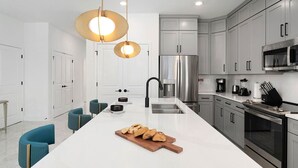 Une cuisine moderne dotée d’un îlot central, d’appareils électroménagers en acier inoxydable et de chaises de couleur turquoise.