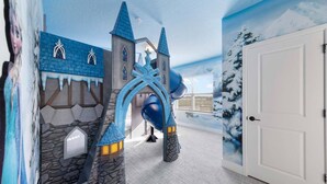 Un espace de jeux avec un toboggan, des murs décorés sur le thème du château et une porte.