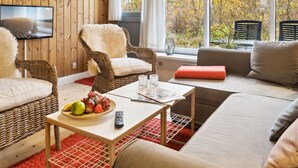 A cozy living room with a television, wicker chairs, a sofa, and a table with fruit and a remote control. - "Rubi" - 250m from the sea by Interhome (Væggerløse)