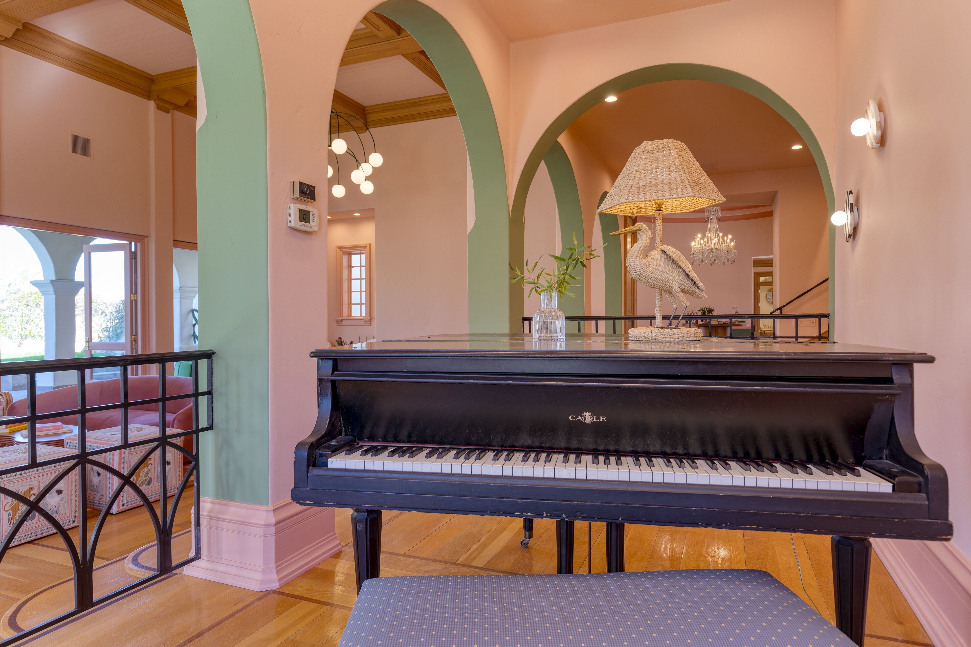 A grand piano in a room with green arches and a chandelier.