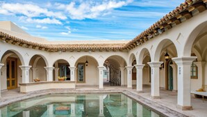 A courtyard with a pool, arches, and a tiled roof.