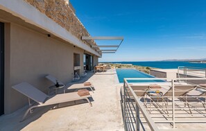 Área de piscina no terraço com espreguiçadeiras e vista para o mar.