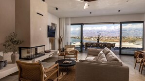 Ein geräumiges Wohnzimmer mit großem Fenster und Blick auf die Berge, Deckenventilator und flachbildschirm-Fernseher an der Wand.