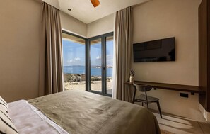 Habitación de hotel con cama, escritorio, silla, televisión de pantalla plana y un amplio ventanal con vista al mar.