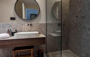 Un baño moderno con un espejo redondo, un lavabo blanco y una zona de ducha.