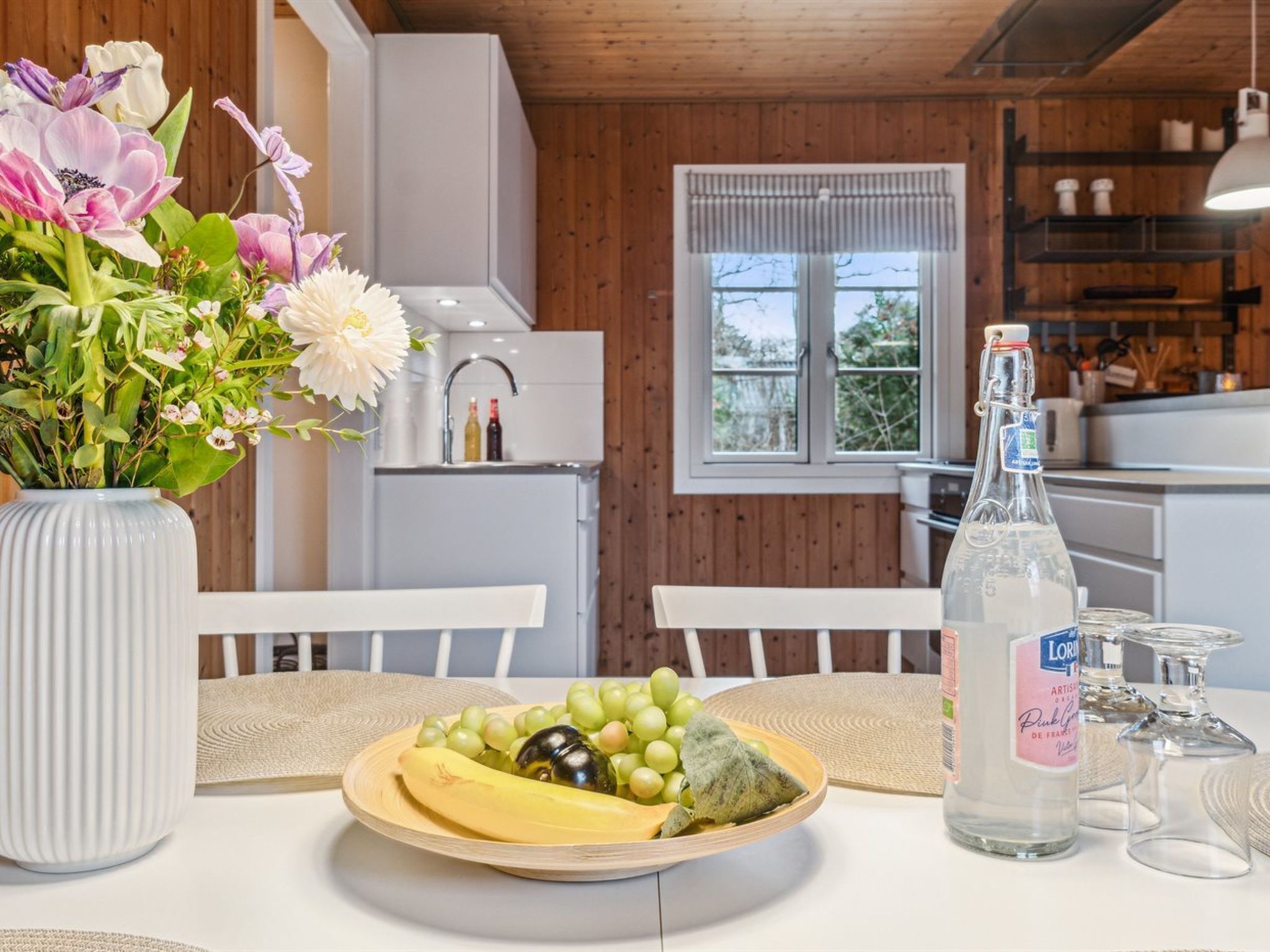 En matplats med ett bord dukat för en måltid, en vas med blommor och en flaska vatten.
