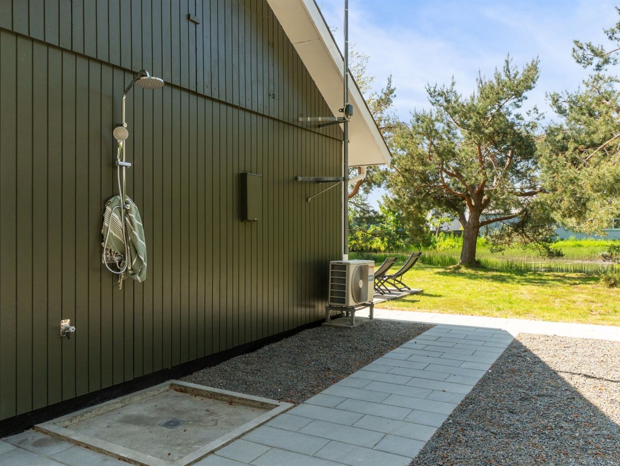Un bâtiment à l’extérieur métallique, un espace extérieur abrité avec un banc, et un arbre en arrière-plan.