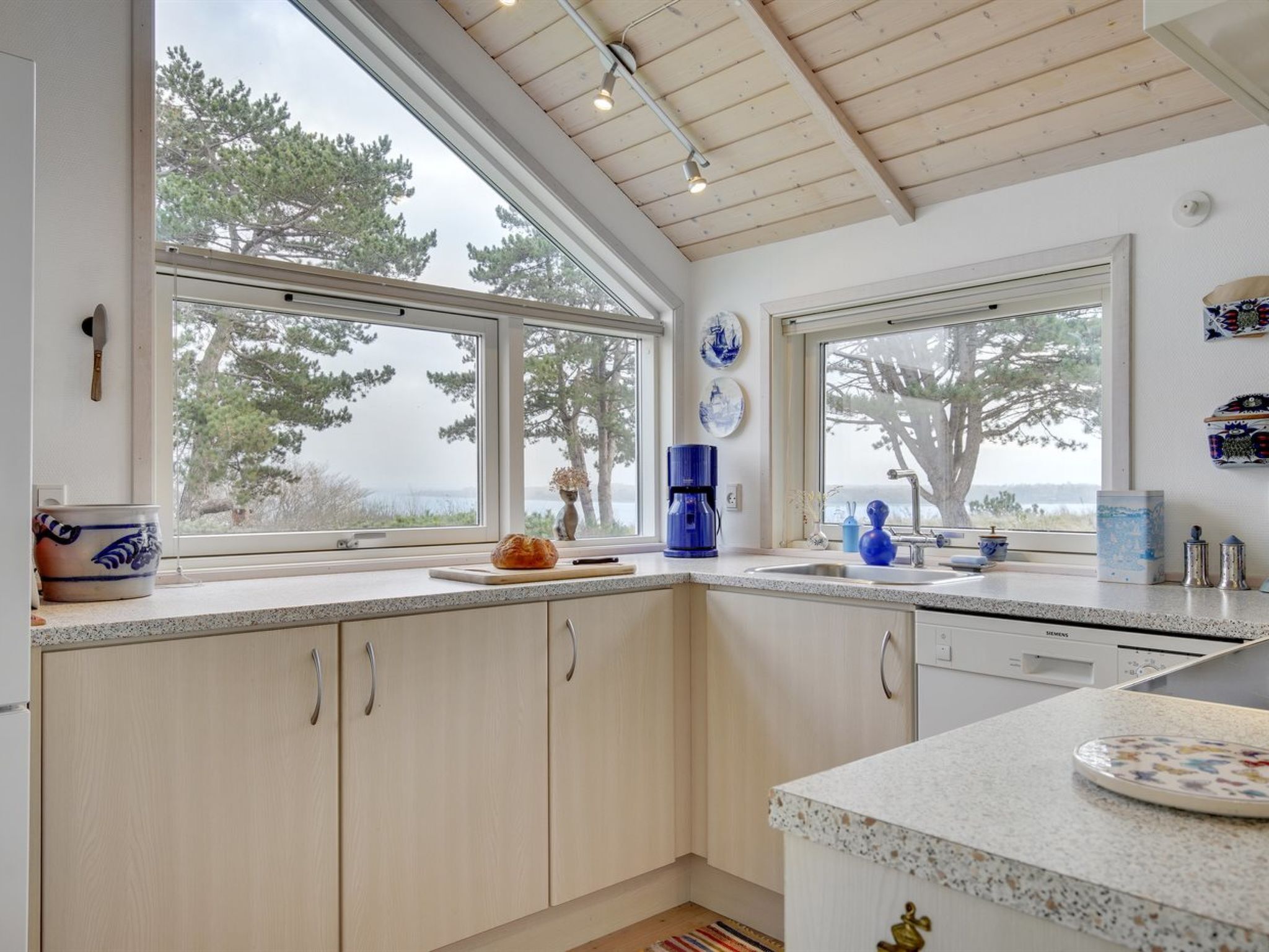A modern kitchen with large windows, wooden cabinets, and a granite countertop.