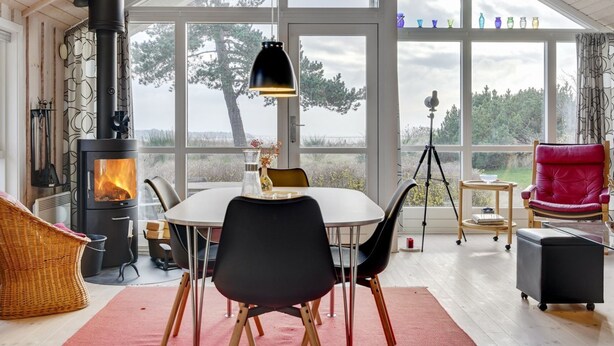 A cozy room with a large window, a fireplace, a dining table, and a red chair. - "Bosilka" - 75m from the sea by Interhome (Hundested)