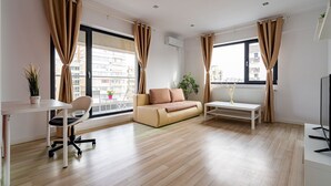 Ein modernes Wohnzimmer mit einer Couch, einem Couchtisch, einem Schreibtisch mit Stuhl und großen Fenstern mit Vorhängen.