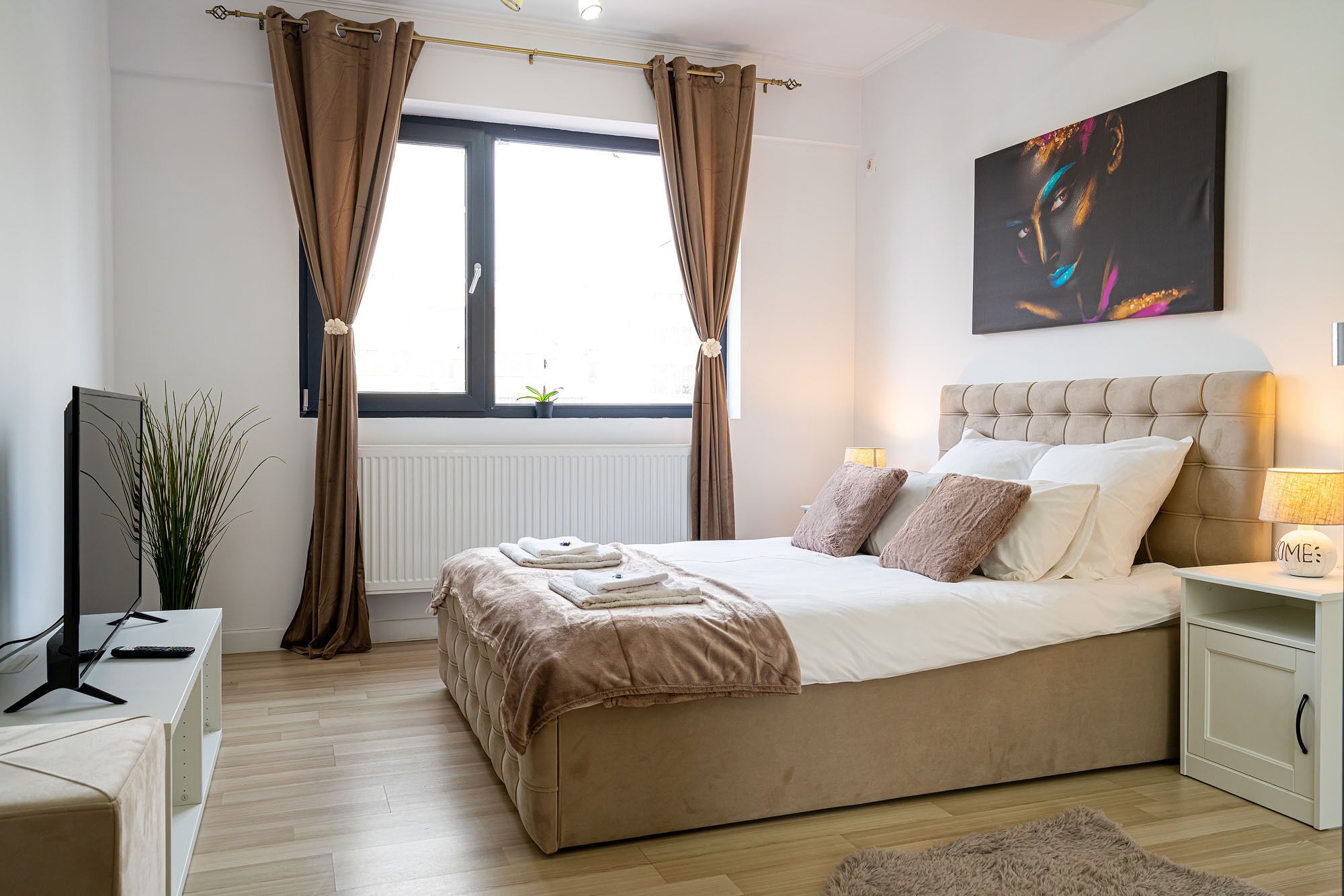 A bedroom with a bed, bedside table, lamp, and a painting on the wall.
