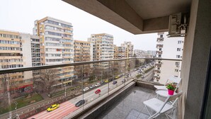 Ein Balkon mit Blick auf eine Stadtlandschaft, mit mehreren Wohngebäuden und einer belebten Straße mit Autos.