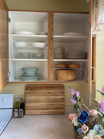A kitchen with a wooden cabinet, a countertop with a cutting board, and a vase of flowers.