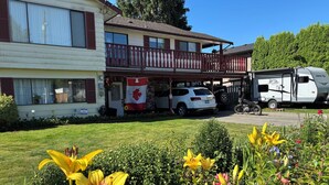 A two-story building with a balcony, a parked white SUV, and a recreational vehicle in the driveway. - Clean safe double bedroom, comfy bed, keyless entry, no stairs, on bus routes (Langley Township)