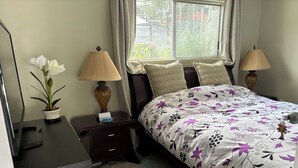 A neatly arranged bedroom with a bed, two bedside tables, a lamp, a potted plant, and a window with blinds. - Clean safe double bedroom, comfy bed, keyless entry, no stairs, on bus routes (Langley Township)