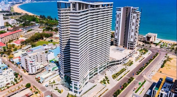 A high-rise hotel with a curved facade, located near a beach and a coastal road.