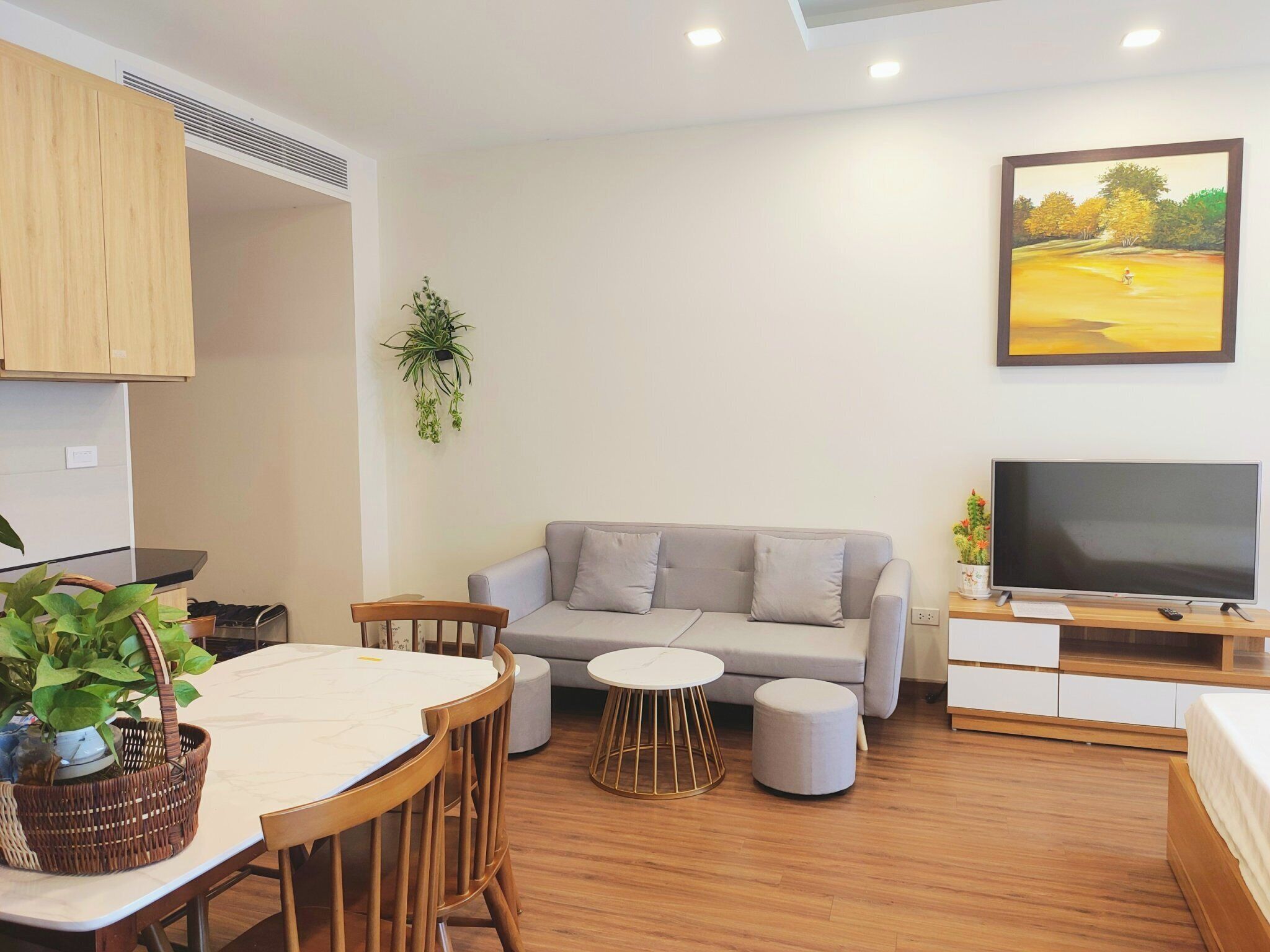 Uma sala de estar moderna com um sofá cinzento, uma mesa de jantar com cadeiras, uma TV sobre um suporte de madeira e um quadro na parede.