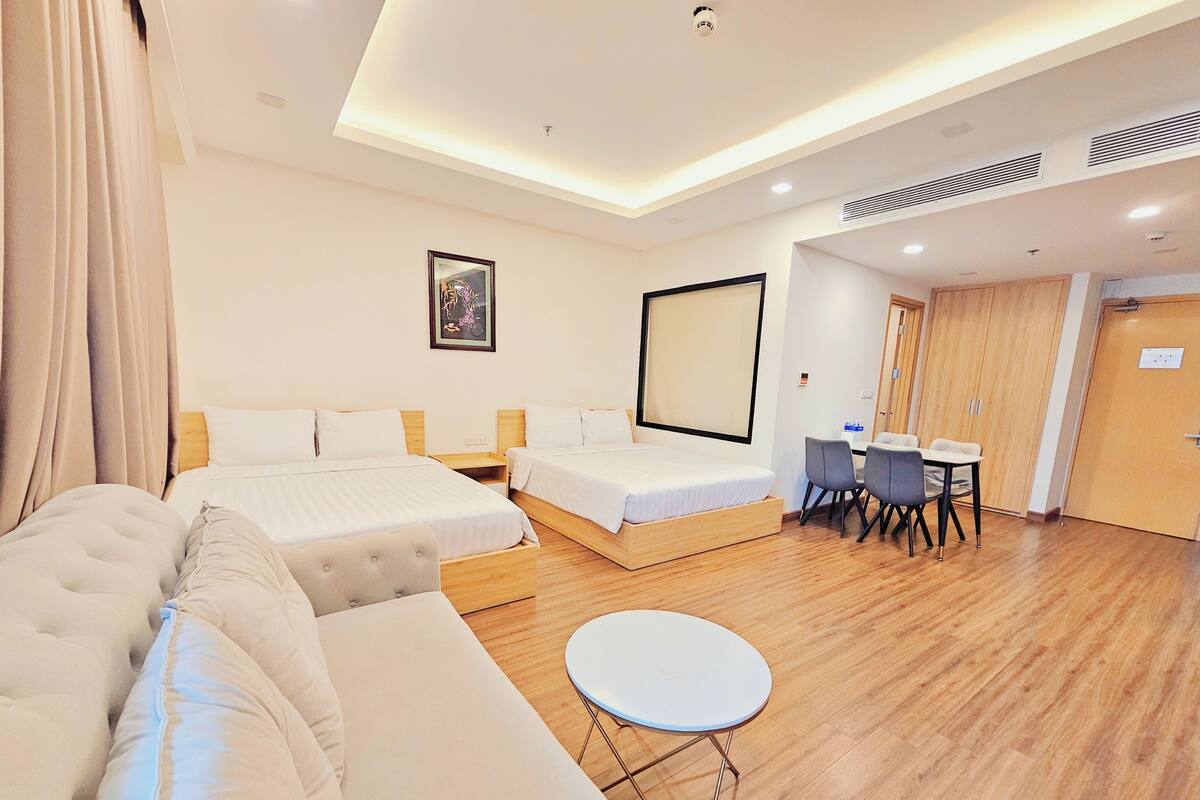 A hotel room with two beds, a sofa, a small table, and a desk with chairs.
