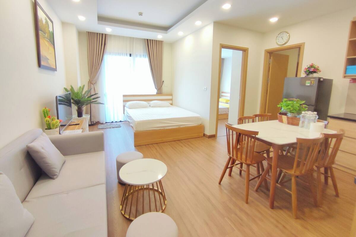 A modern hotel room with a bed, a sofa, a dining table with chairs, and a small round table.