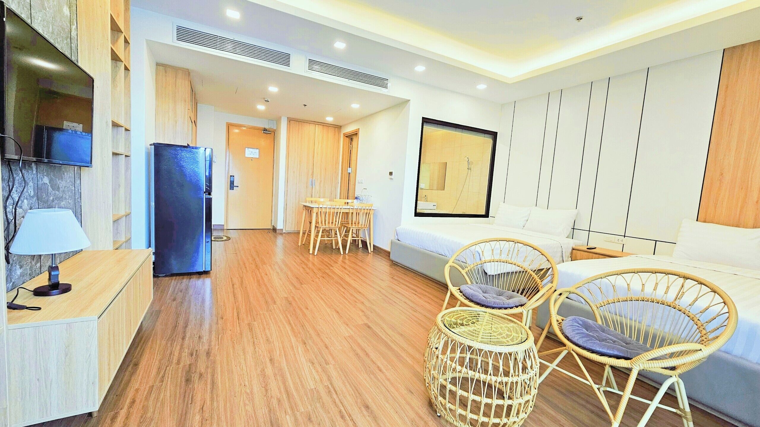 Una habitación de hotel moderna con suelo de madera, un área de comedor con mesa y sillas, una cama con cabecera y un televisor montado en la pared.