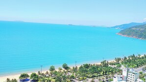 A coastal view with a beach, palm trees, and buildings along the shore. - FLC SEA TOWER QUY NHƠN BEACH (Quy Nhon Nam)