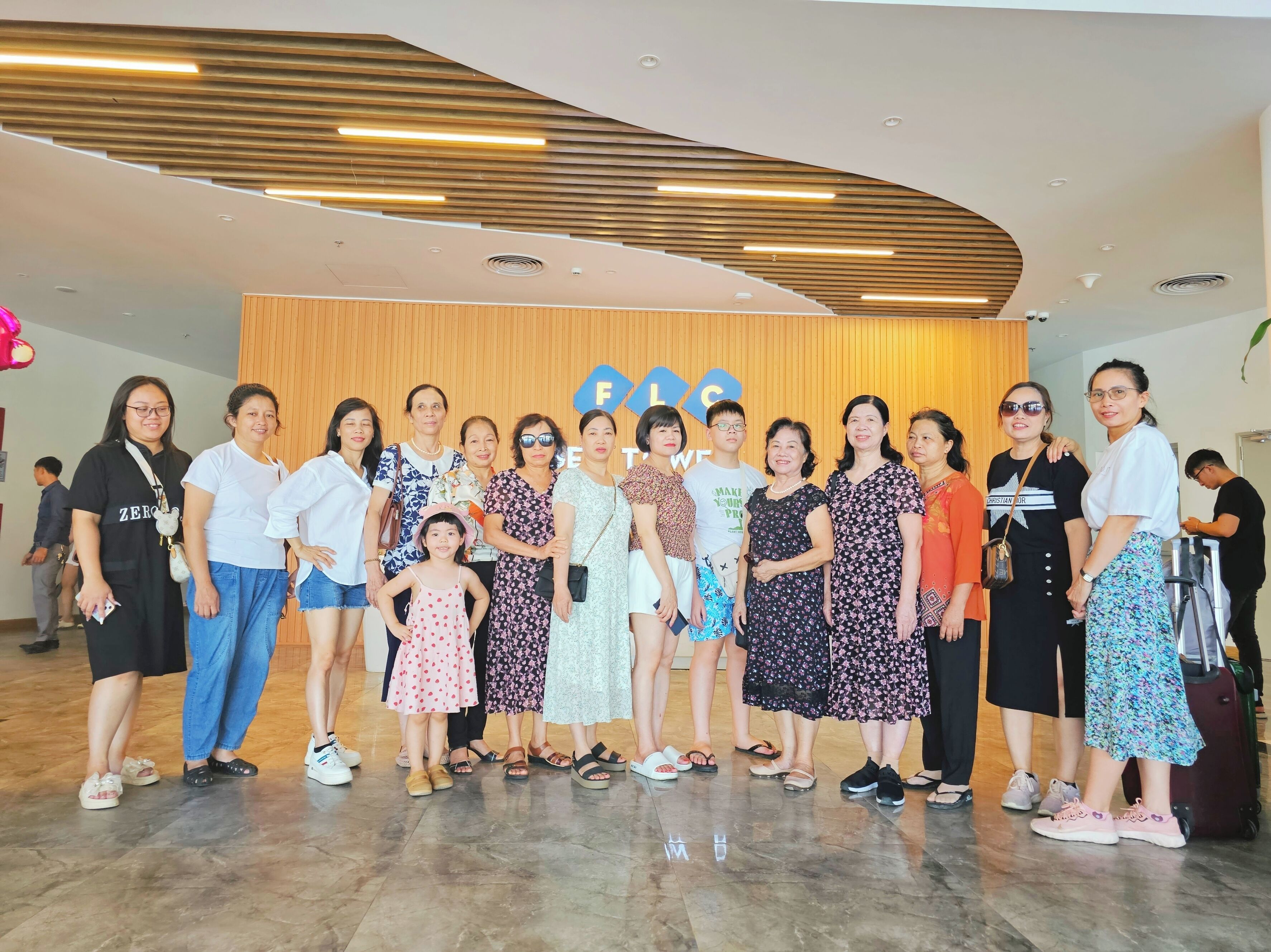 A group of people standing in a lobby with a wooden panel wall and a sign with letters.