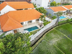 A residential property with a swimming pool, a garden, and a view of a rice field.