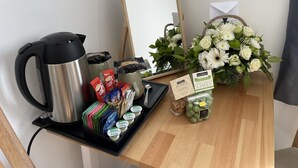 A kitchenette with a coffee maker, tea bags, milk cartons, and a flower arrangement on a wooden table.