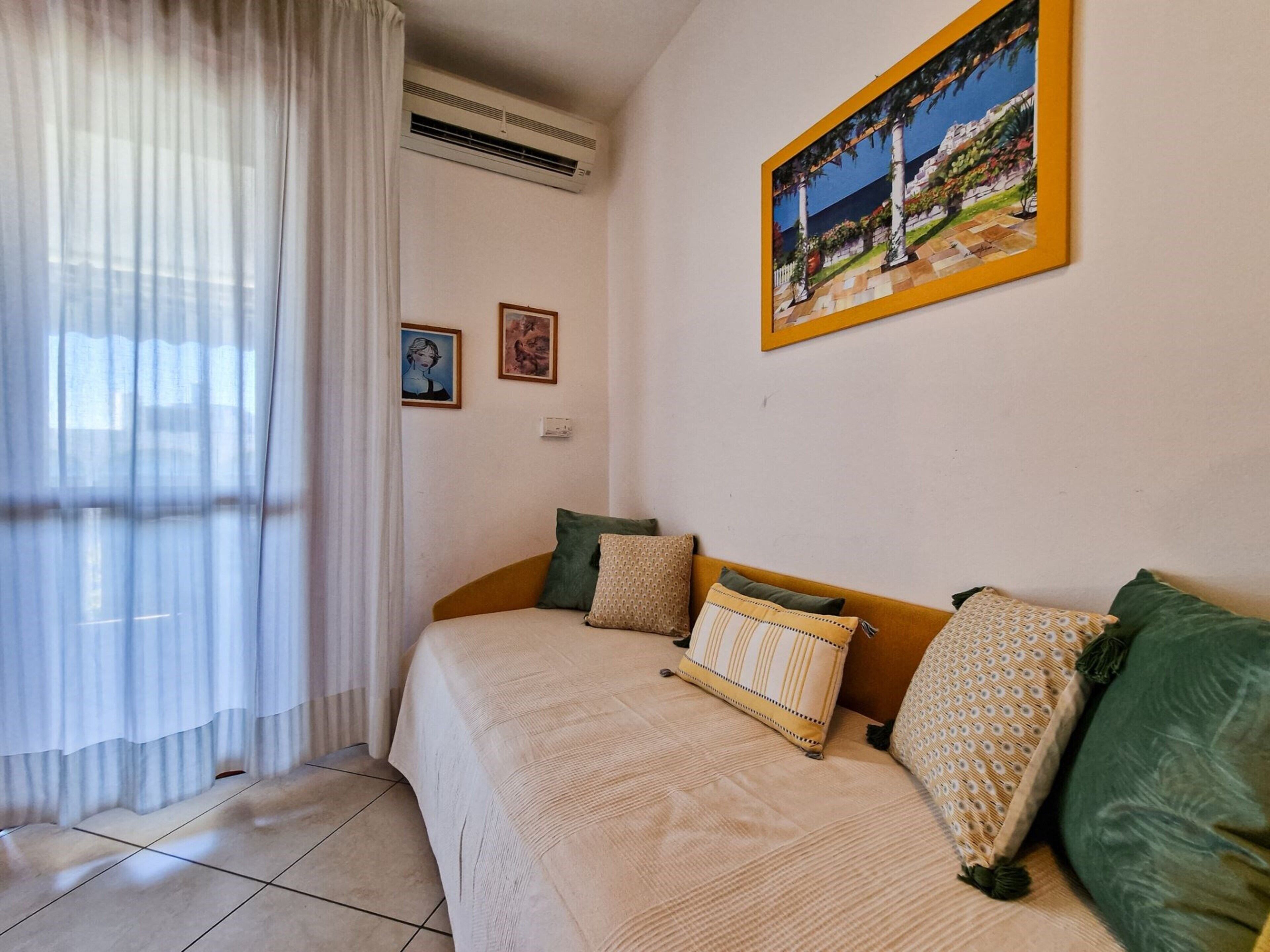 A bedroom with a bed, a painting, and a window with curtains.