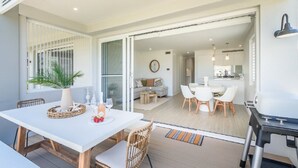 A modern dining area with a white table, wicker chairs, and a grill station. - Stay 3 nights, pay 2 this Winter* (BOOKER BAY)