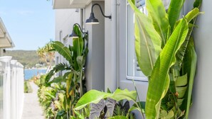 A narrow pathway lined with lush tropical plants and a white building with a window and a wall-mounted lamp. - Stay 3 nights, pay 2 this Winter* (BOOKER BAY)