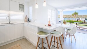 A modern kitchen with white cabinetry, a central island with bar stools, and a view of the marina through large windows. - Stay 3 nights, pay 2 this Winter* (BOOKER BAY)